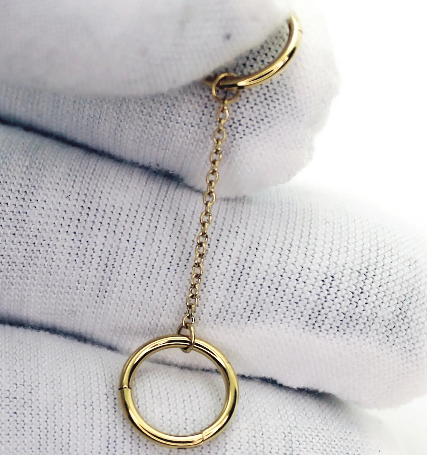 Présentation d'un bijou de piercing en titane composé d'un double anneau relié par une chainette. Version PVD Or présentée sur des gants en coton