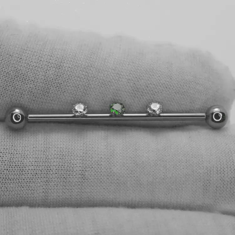 Présentation d'une barre de piercing pour industriel avec 2 pierres de zircon blanches et 1 pierre verte pour une longueur de barre de 36 mm