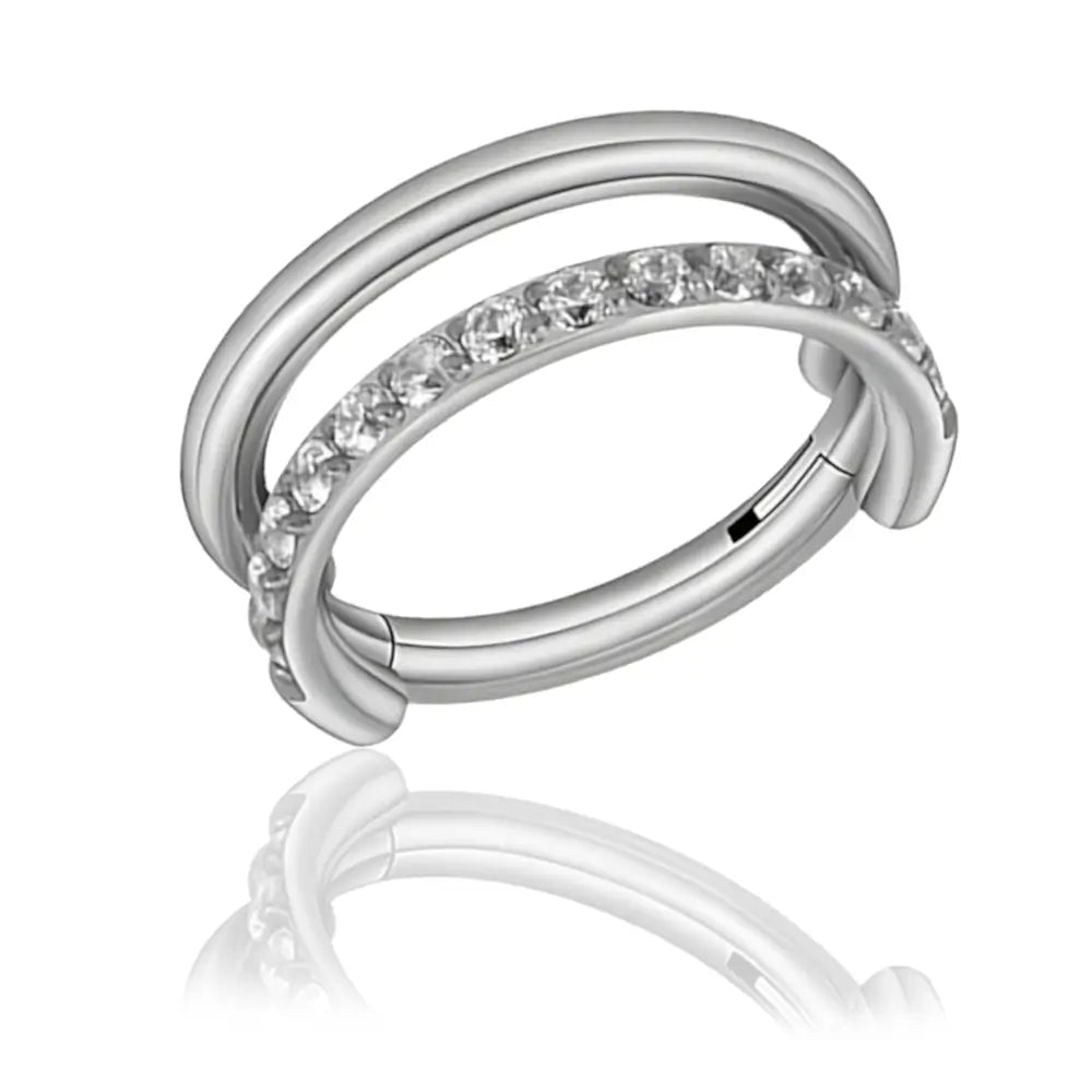 L'image présente l'anneau double Ravélia en titane avec sa fermeture à charnière clicker. L'anneau est orné d'une pierre de zirconium scintillante qui ajoute une touche d'élégance. La finition argentée du titane met en valeur le design moderne et sophistiqué de cet anneau pour helix.