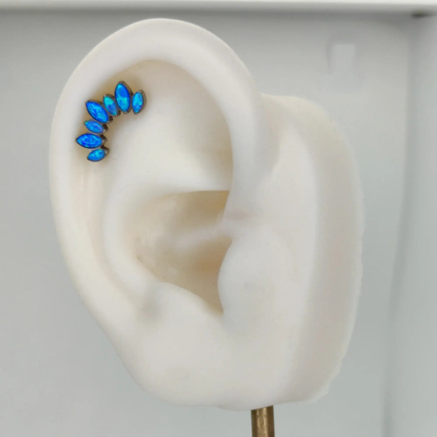 Piercing en titane avec opale bleue, présenté sur l'hélix d'un oreille artificielle