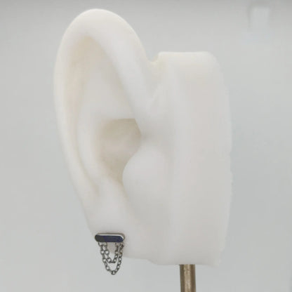 Piercing en titane avec chainette, présenté sur le lobe d'une oreille artificielle